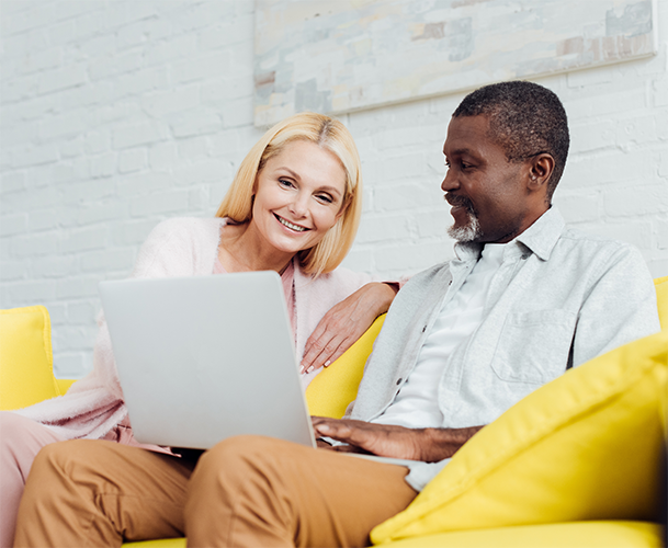 couple on yellow couch discussing tax strategies for investment with laptop